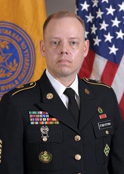 Photo of man in US Army uniform in front of flags